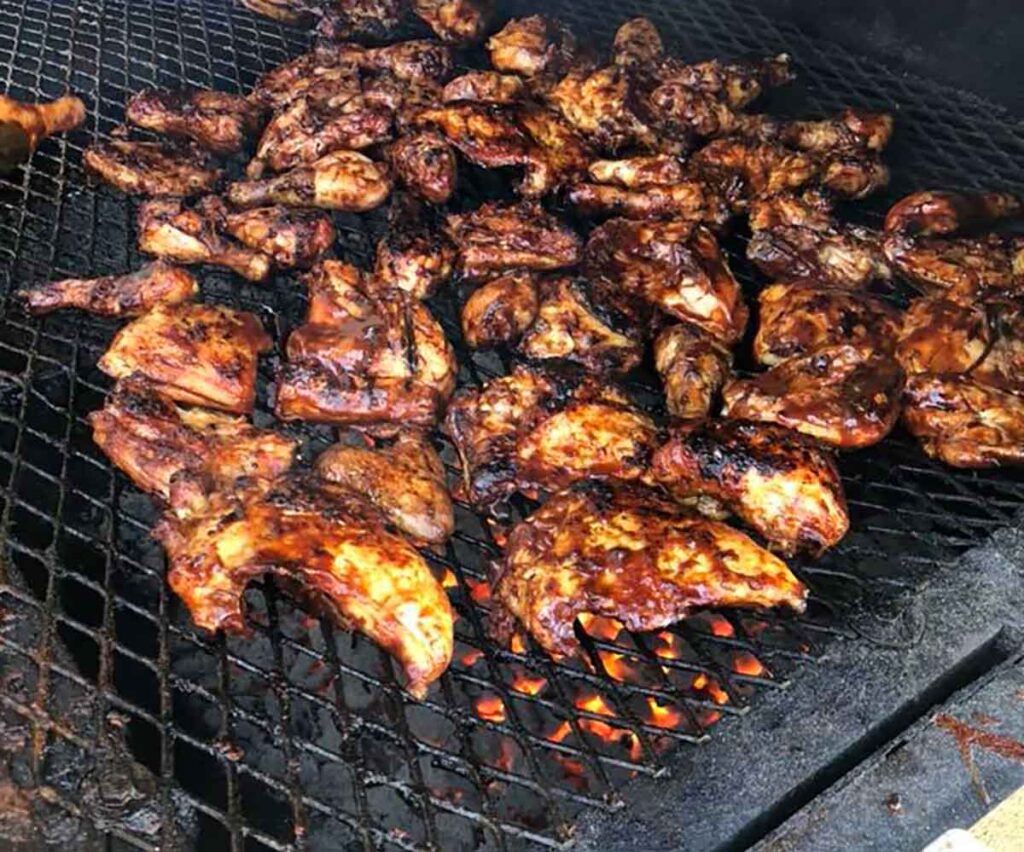 Barbecued chicken on grill with glowing embers below