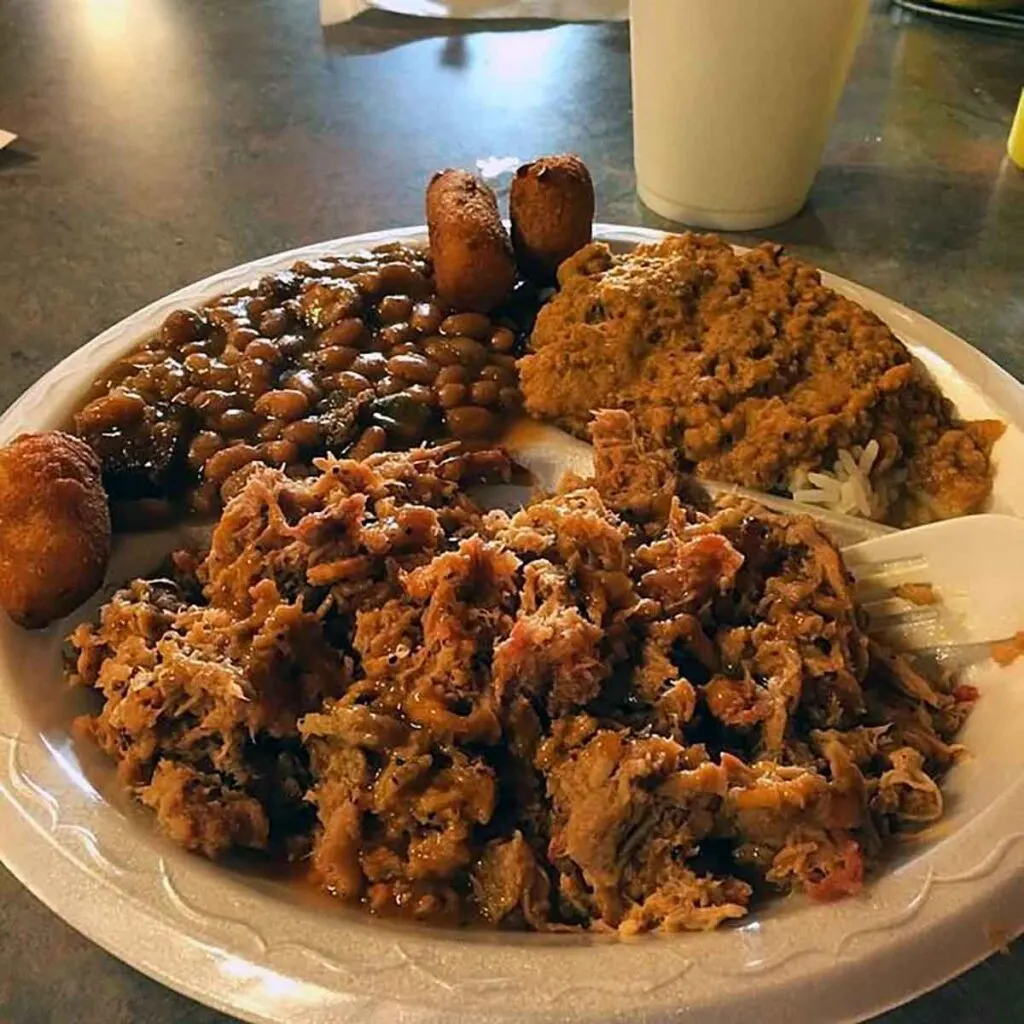 Plate loaded with chopped BBQ, baked beans, hash and hushpuppies