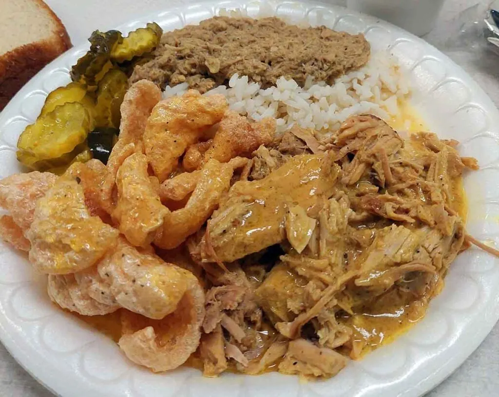 Plate of barbecue, pork rinds, rice and hash, and pickles
