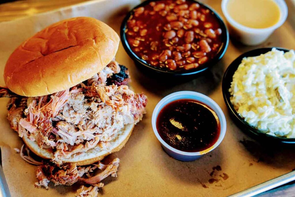 BBQ sandwich and sides on metal tray with sauce.