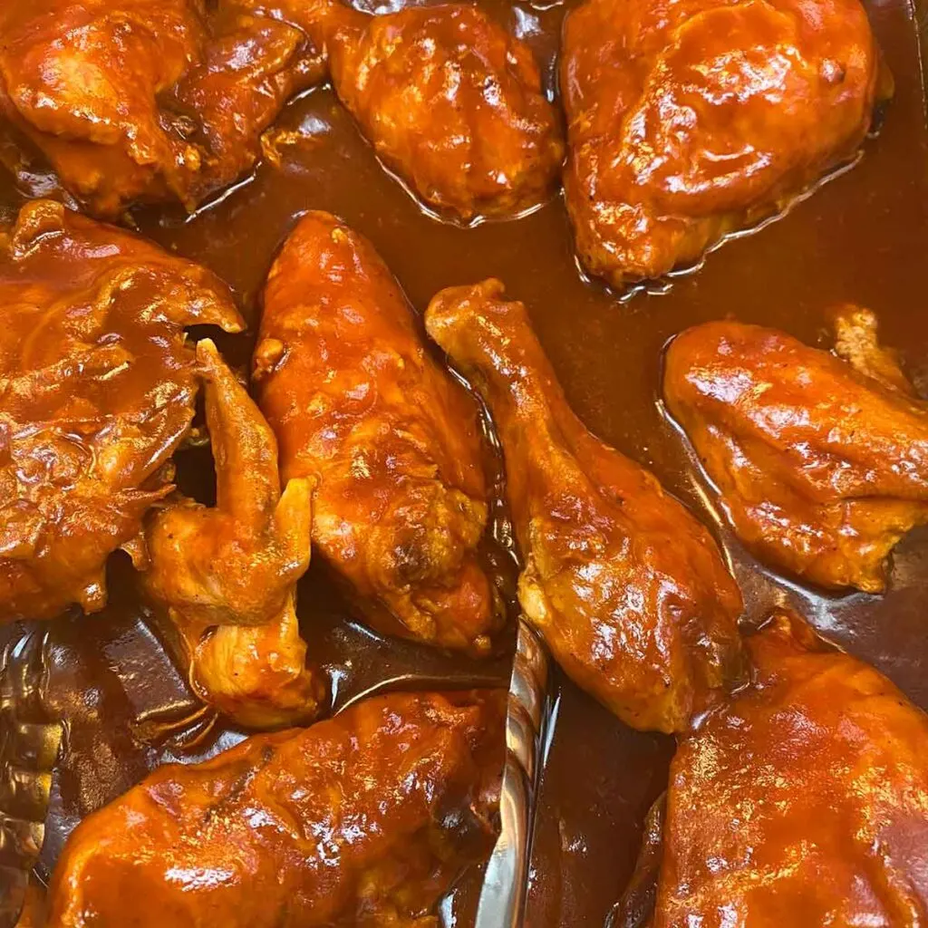 Pan full of barbecued chicken resting in a red sauce.