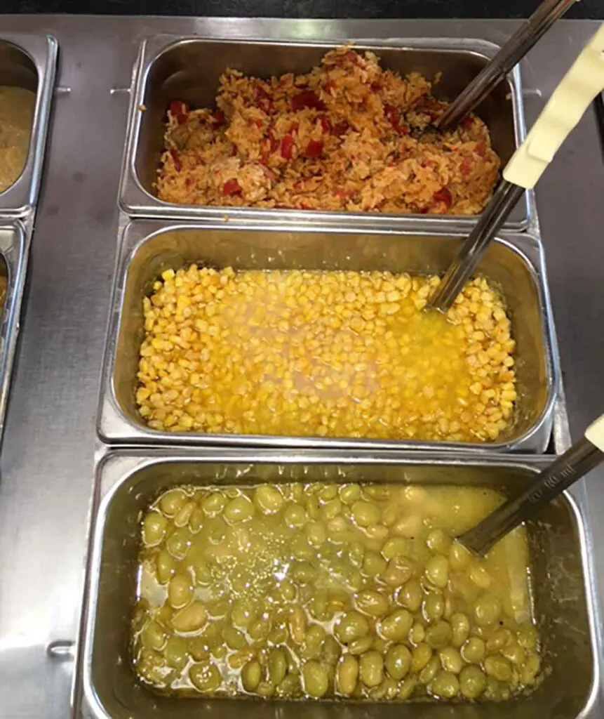 Red rice, corn, and butter beans in trays on buffet.