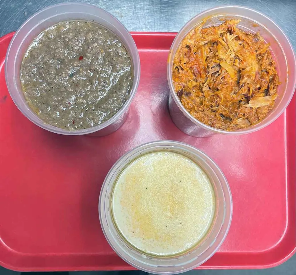 To Go containers of beef hash, barbecue, and chicken stew on read plastic tray