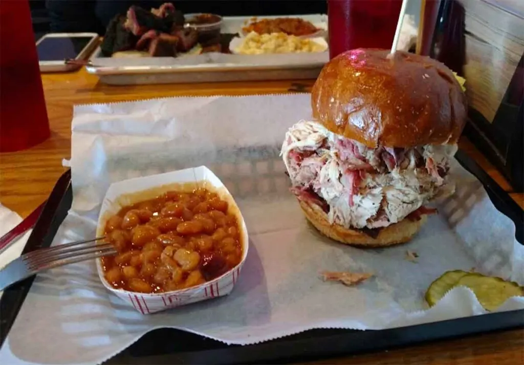 Heaping barbecue sandwich with paper tray of baked beans