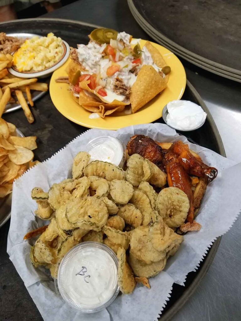 Basket of fried pickle chips with other foods in background