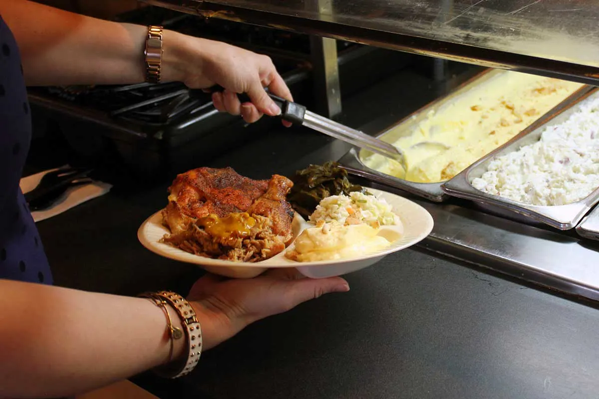 Closeup of hand spooning food from buffet with plate of food in other hand.