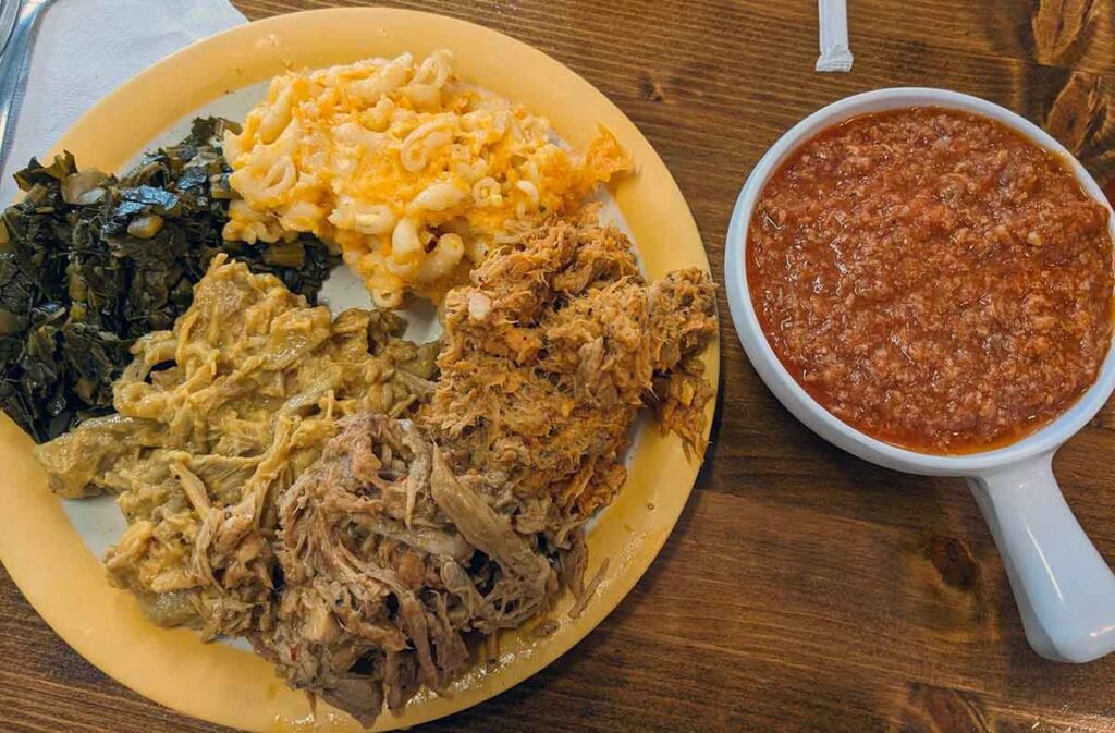 Plate of barbecue and sides with hash in a bowl to the side.