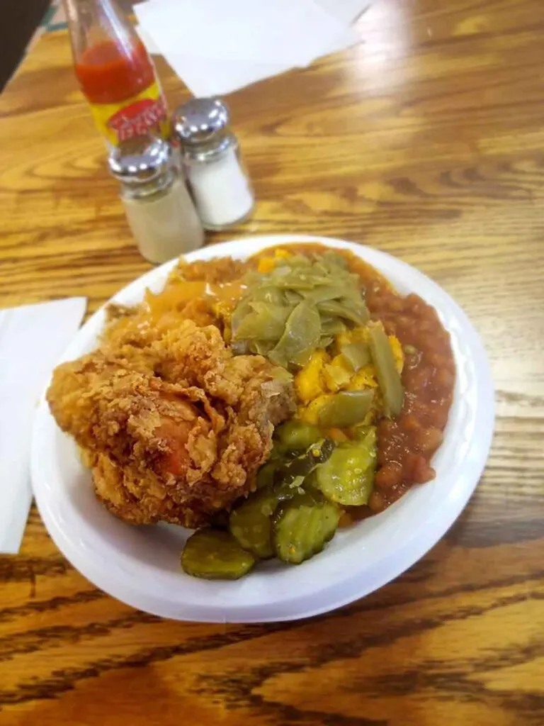 Plate with fried chicken, beans, pickles and more sides.