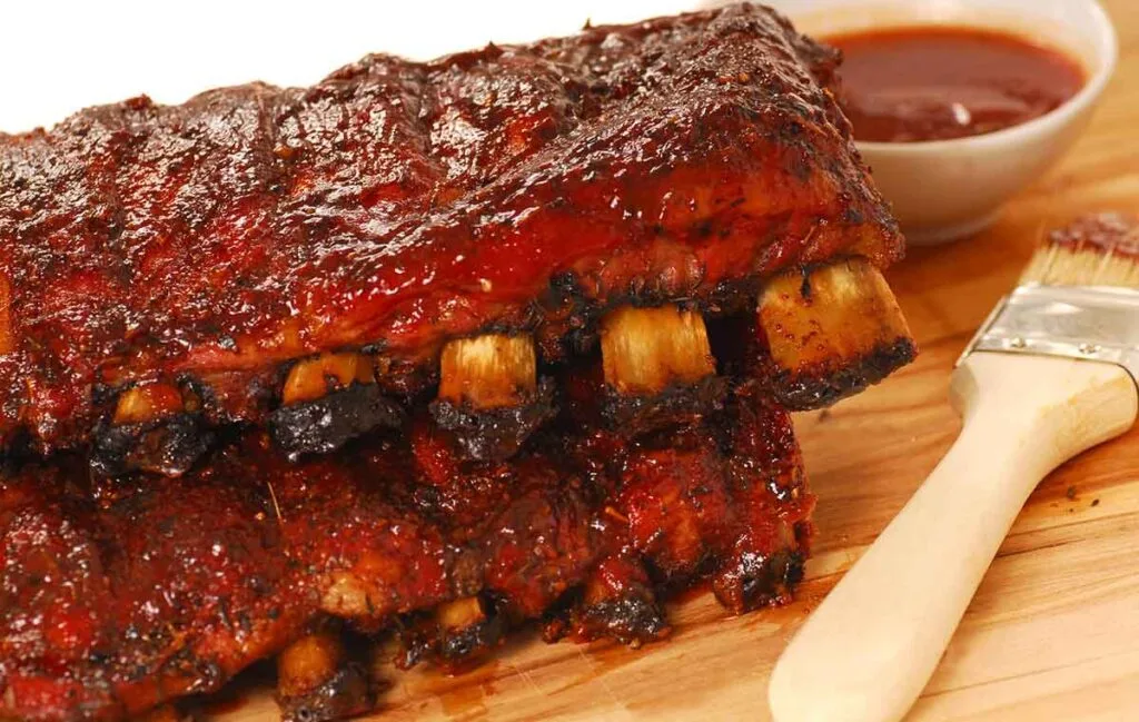 Two hickory smoked rack of ribs with brush and cup of sauce.