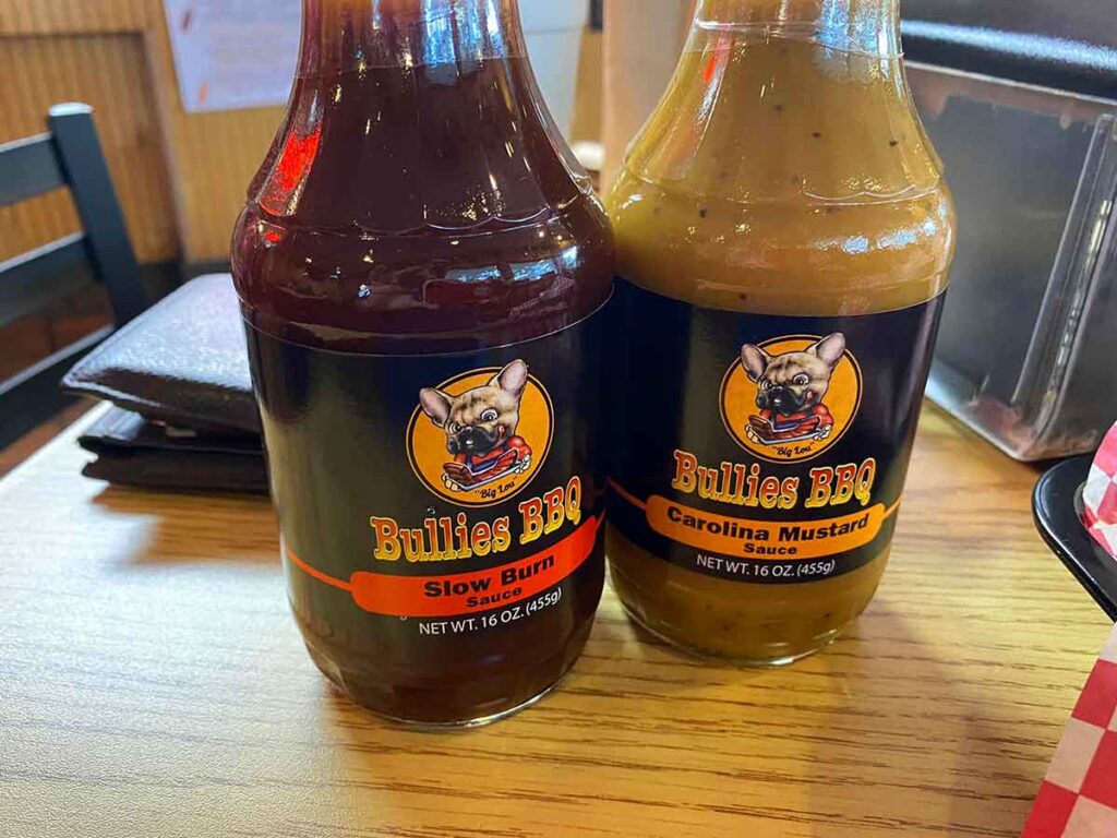 Two bottles of Bullies BBQ  sauces on table.