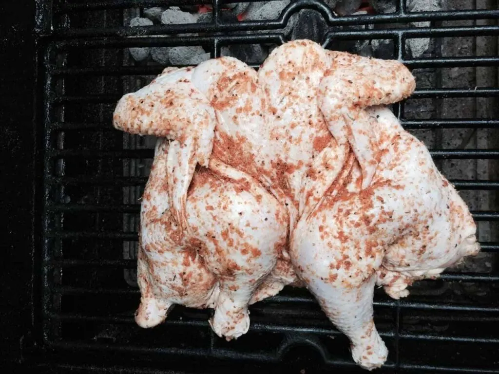 Spatchcocked chicken on a grill coated with Carolina Charcoal rub, ready for cooking.
