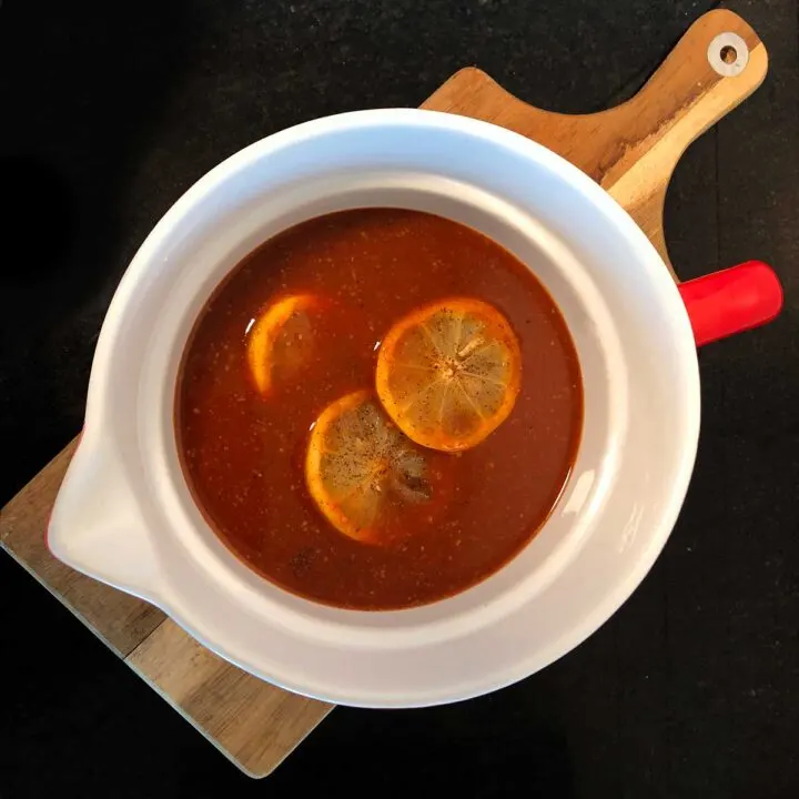 Brisket Mojo Sauce from above with lemons floating in center of bowl on cutting board