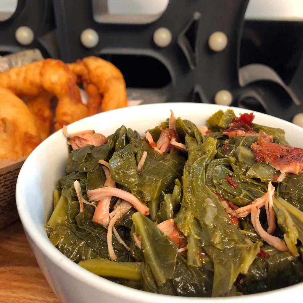 Bowl of Melvin's collard greens with onion rings in background