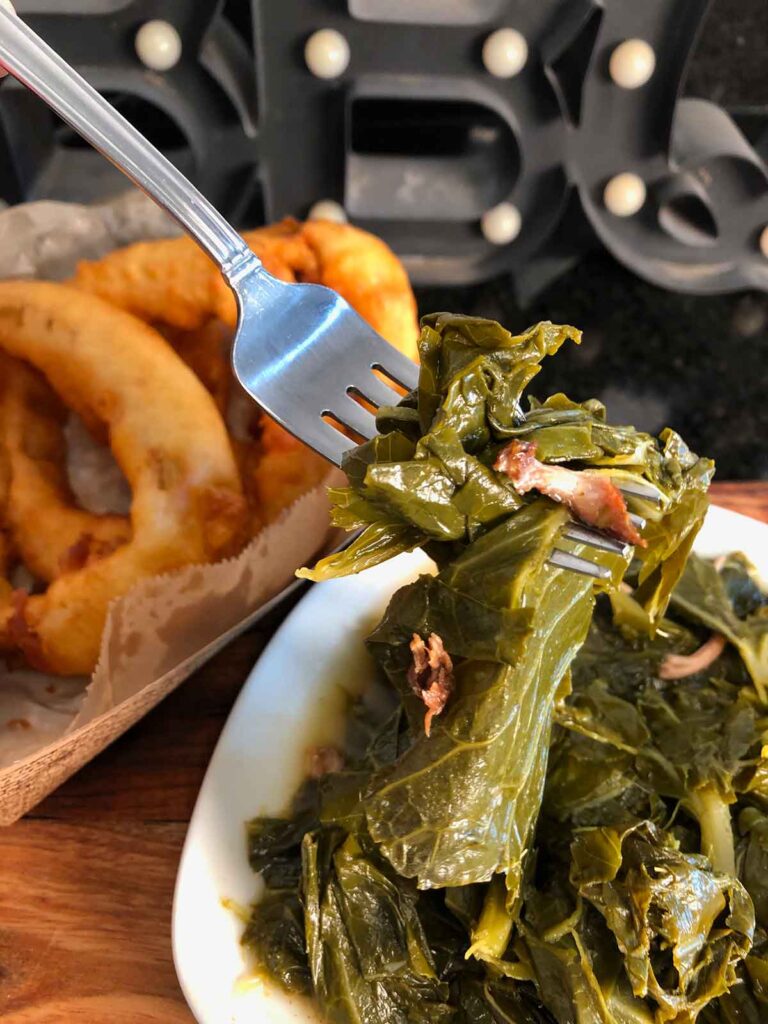 Forkful of Melvin's collard greens with onion rings in background