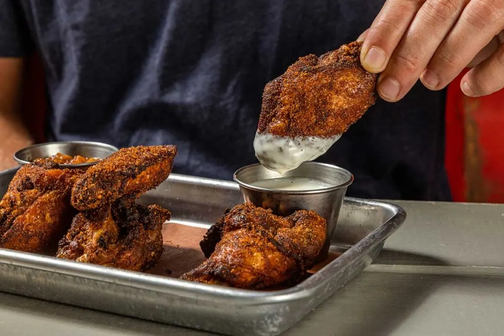 Hand dunking Home Team smoked wing in Alabama White sauce