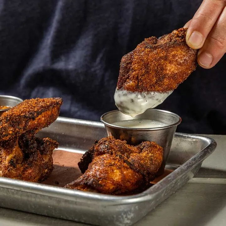 Hand dunking Home Team smoked wing in Alabama White sauce