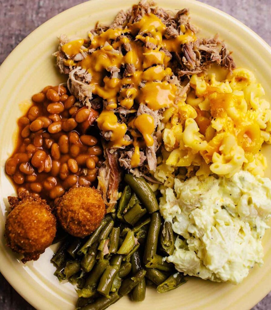 Plate with BBQ and mustard sauce, baked beans, and several other side dishes.