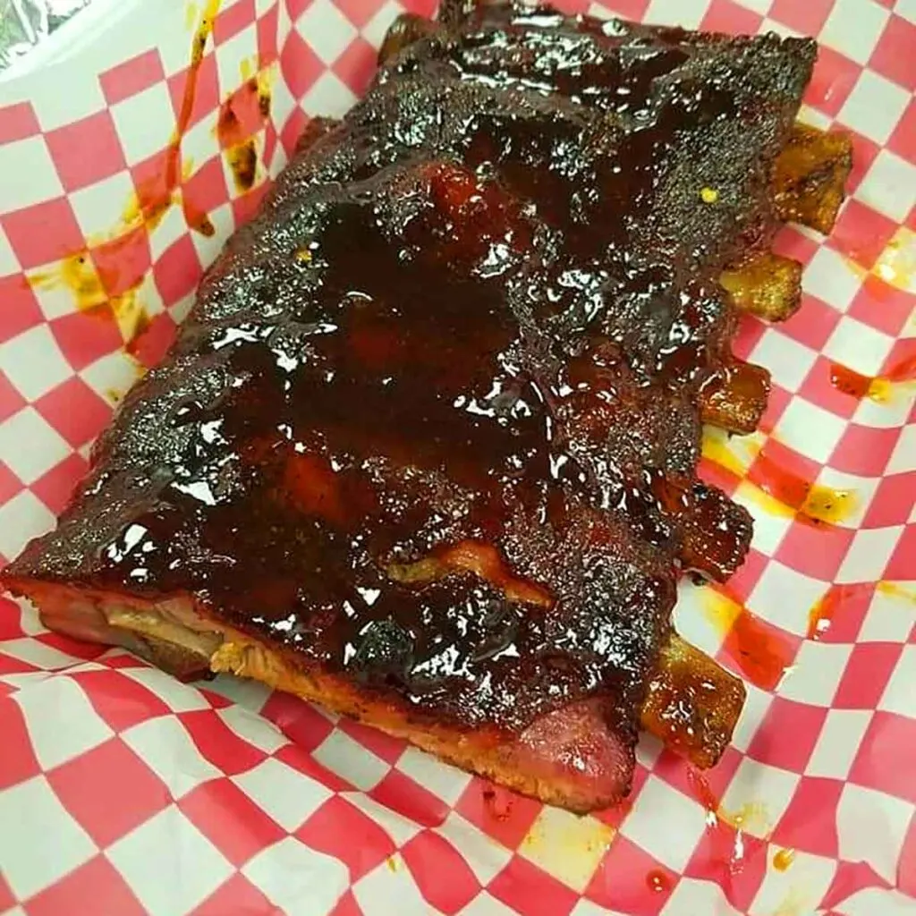 Rack of ribs with sauce on red/white checkerboard paper.