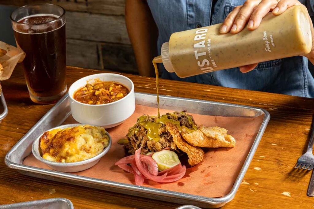 One meat platter with pulled pork, Mac n cheese, and Brunswick stew. Mustard sauce being drizzled on pork.