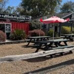 Exterior of Martin's Bar-B-Que on James Island, showing the patio seating area, picnic tables, umbrellas, and Whole Hog BBQ signage.