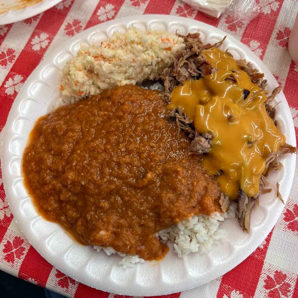 Styrofoam plate with red hash, bbq covered in rust gravy, and slaw.