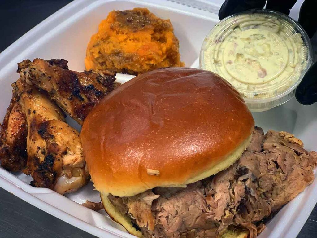 Tray with BBQ sandwich, wings, sweet potato crunch, and container of slaw