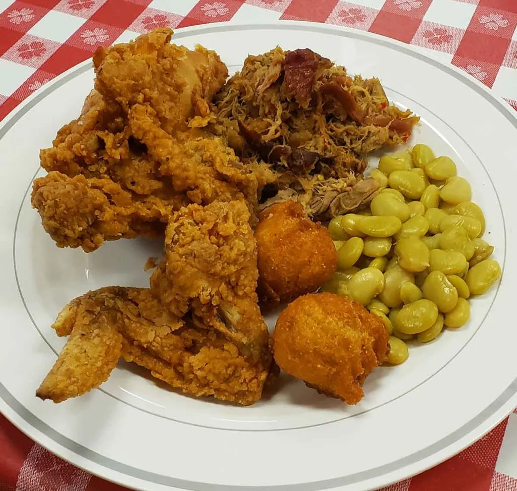 Plate with BBQ, fried chicken pieces, lima beans, and hush puppies.