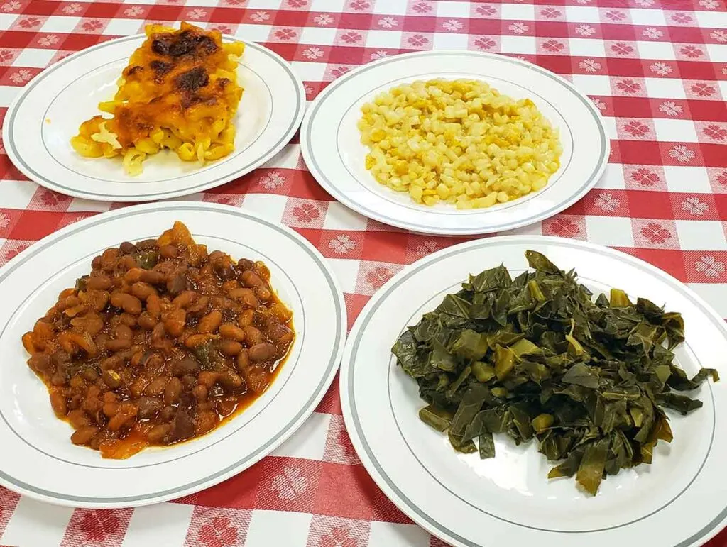 Four plates each with one side: Mac and cheese, corn, baked beans, and green.