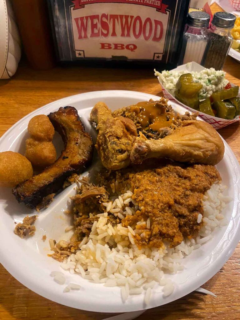 Plate of BBQ and sides on table with hash, chicken, & ribs.