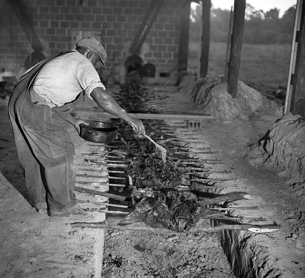 Historic photo of black man working a pit with several pigs over a trench