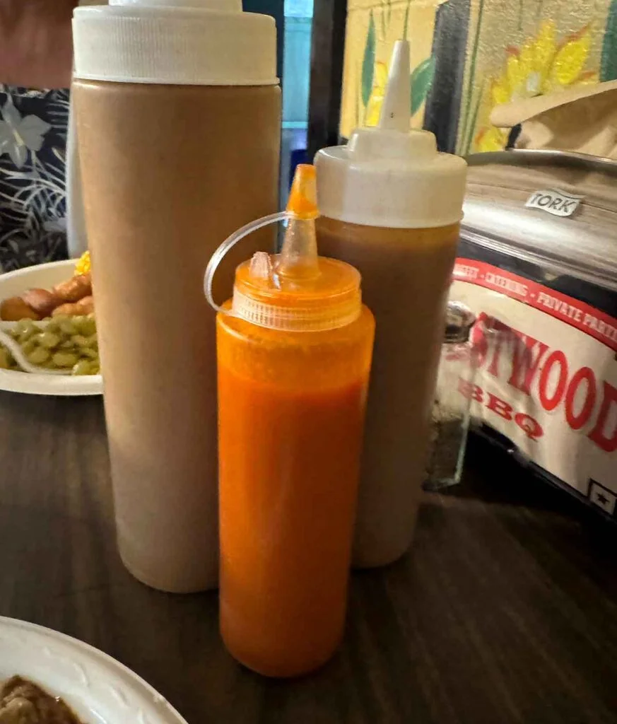 Three plastic squeeze bottles of different sauces on the table beside a napkin dispenser.