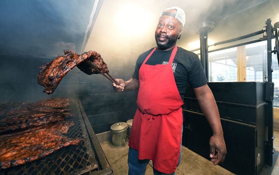 Rodney Scott holding rack of ribs over pit.