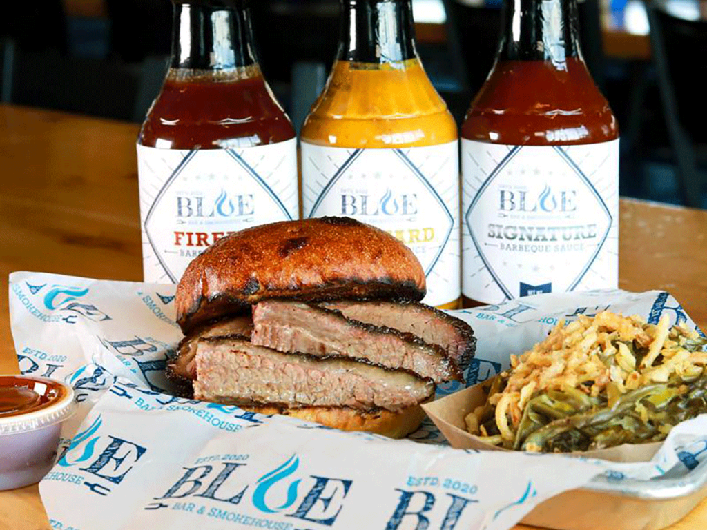 Brisket sandwich with sides and bottles of sauces.