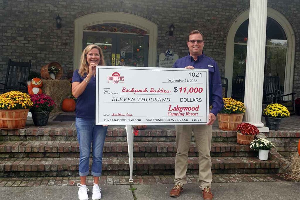 Two people holding a large check for $11,000 made out to Backpack Buddies.