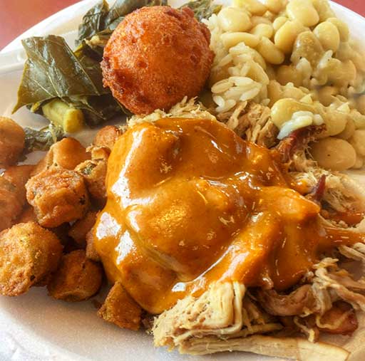 Plate of BBQ covered in mustard sauce with sides at Dukes on James Island