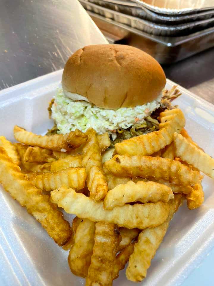 BBQ sandwich topped with slaw and fries in styrofoam tray.