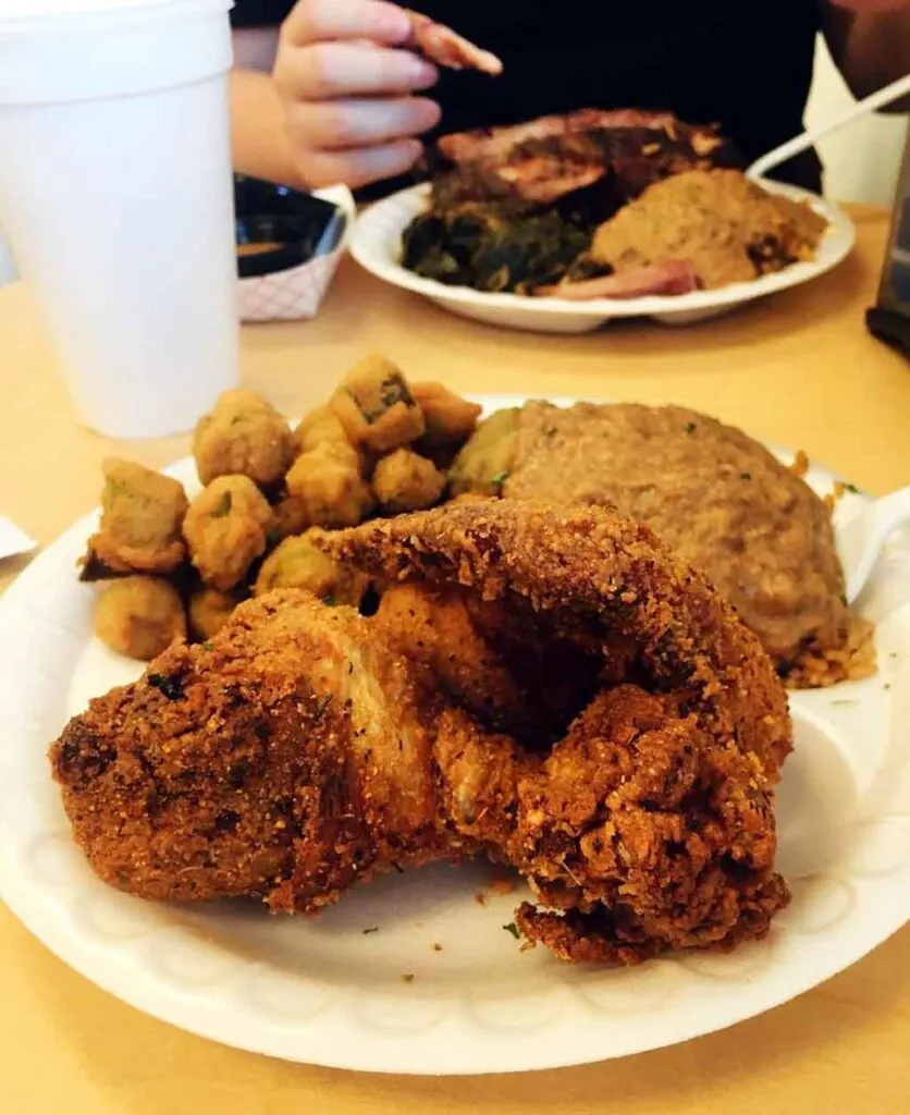 Fried chicken, hash over rice, and fried okra on white styrofoam plate.