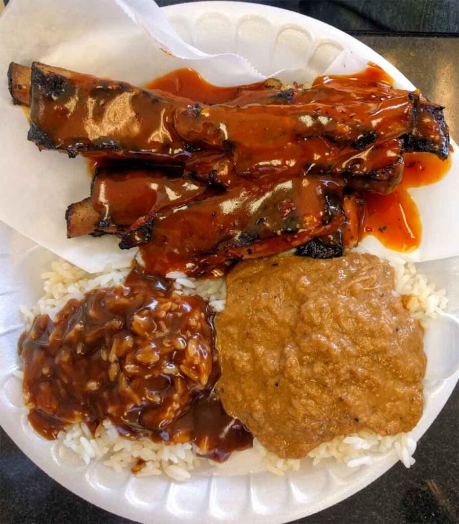 Ribs covered in sauce, hash and rice and rice and gravy on plate.
