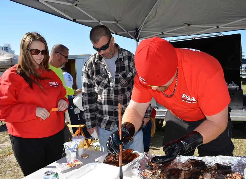 BBQ competitor preps ribs for turn in while his two teammates look on.