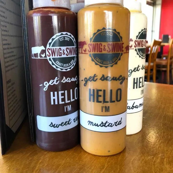 A bottle of Mustard BBQ Sauce in front of two other sauces at Swig & Swine in Summerville.