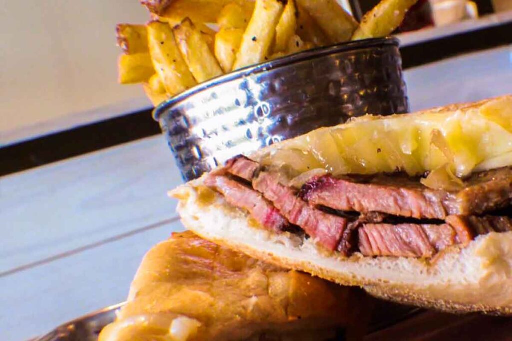 Closeup of Q on Bay's brisket dip sandwich with fries in background