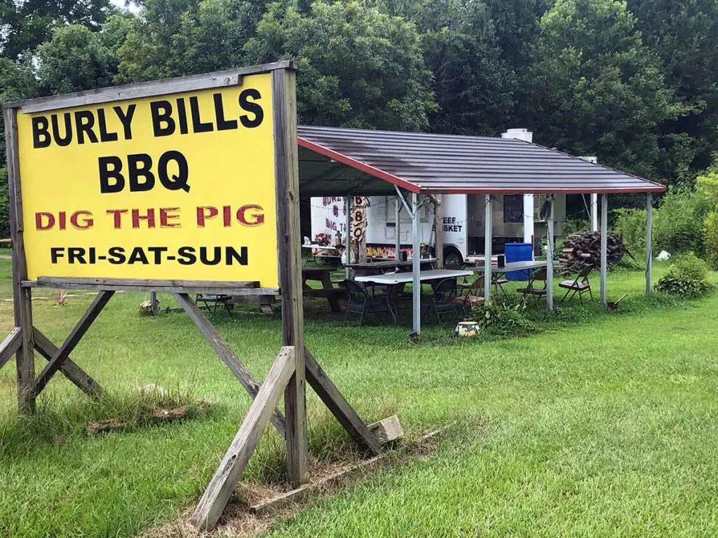 Street view of Burly Bill's BBQ in Marietta showing sign, covered eating area, and food trailer.