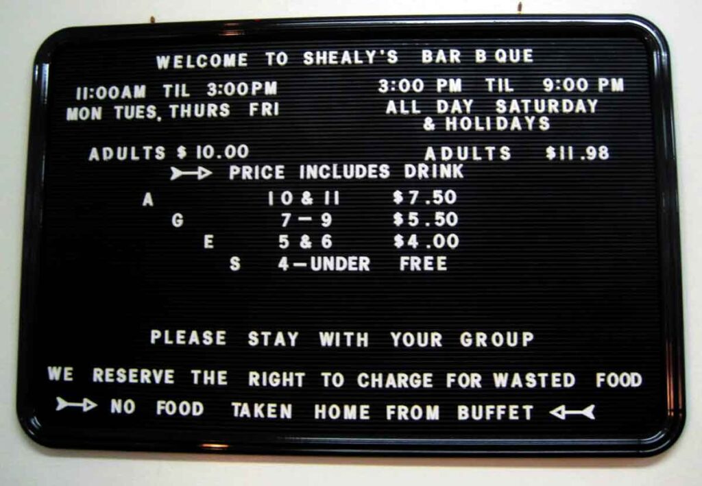Black menu board with days and hours of operation and menu prices for Shealy's BBQ buffet