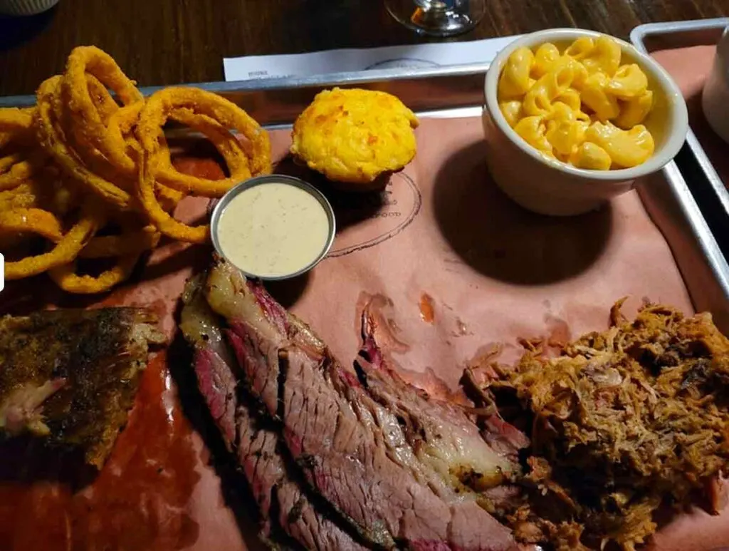 Three meat platter with onion rings, Mac n cheese, sauce and muffin.