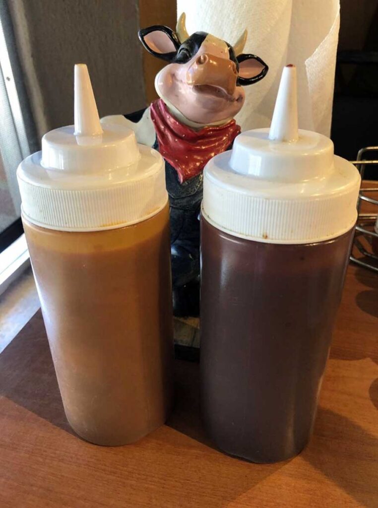 Carolina Gold mustard sauce and a traditional tomato sauce in plastic squeeze bottles in front of happy cow figurine. 