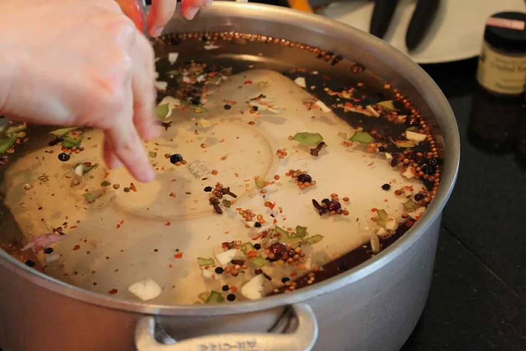 Stock pot full of brine with spices floating on top. Plate is submerging unseen meat for brining.