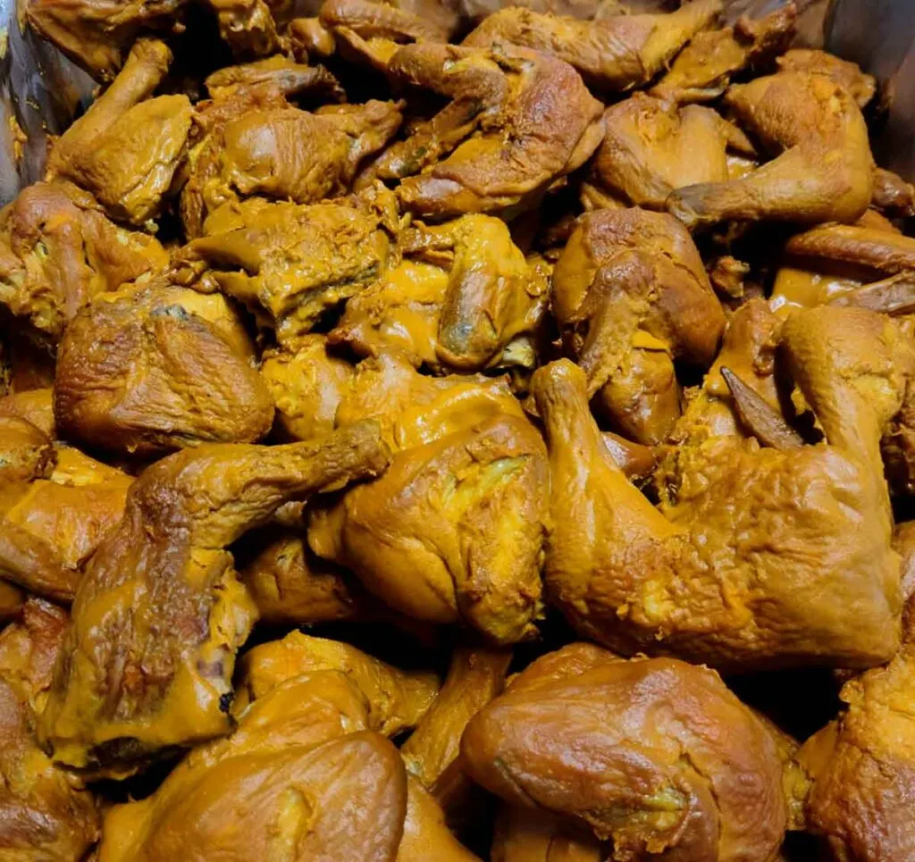 Chicken coated in yellow mustard sauce in buffet pan.