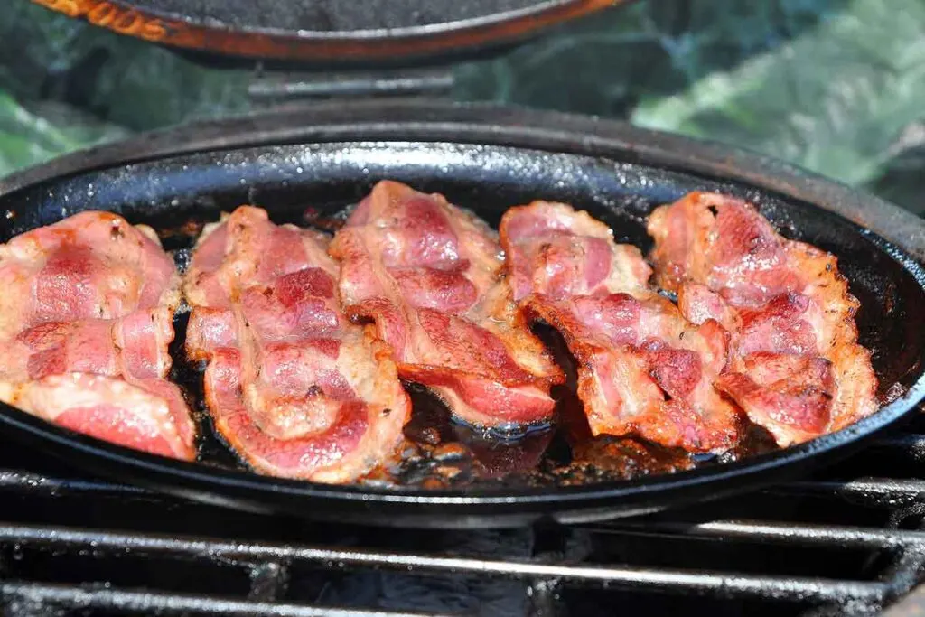 Wild boar bacon cooking in a cast iron skillet