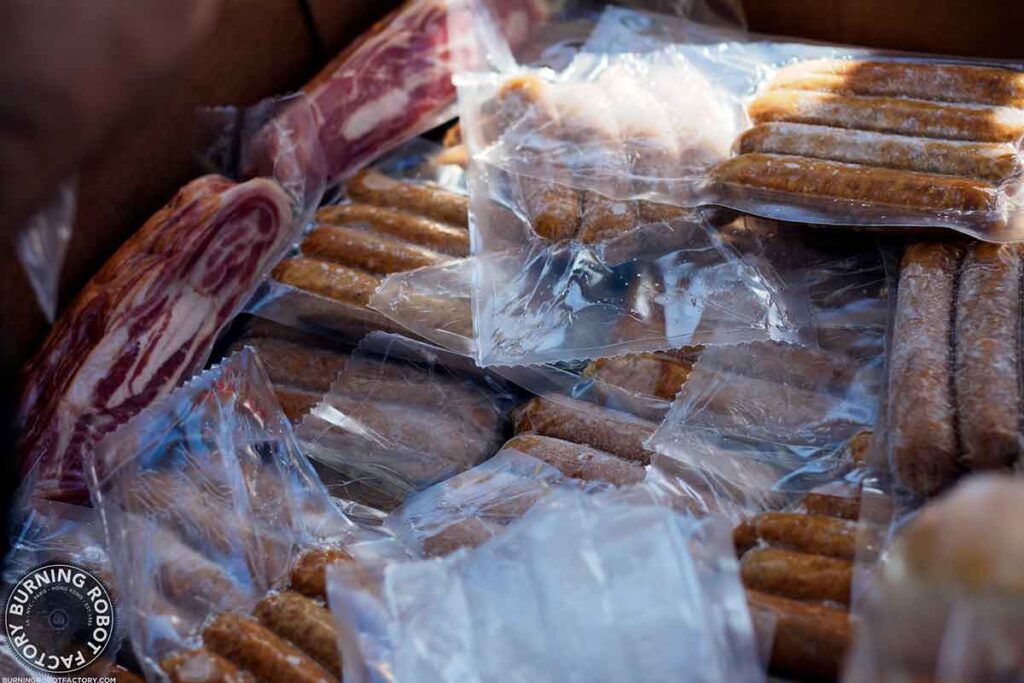 A box of shrink wrapped "exotic" meats including sausages and wild boar bacon.