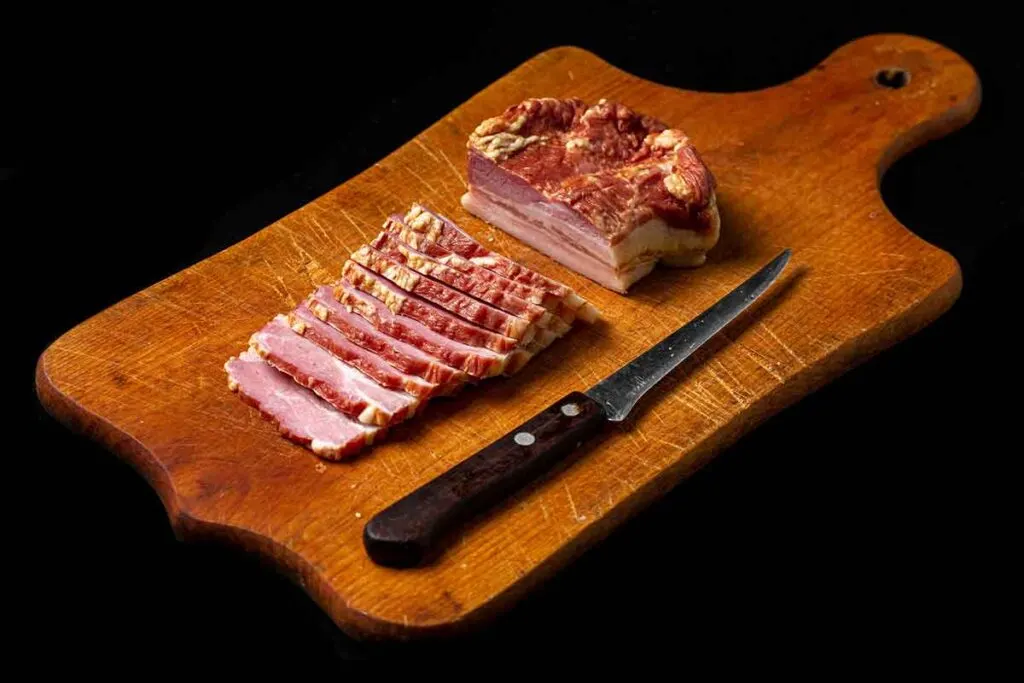 Thick slices of smoked bacon on cutting board with knife.
